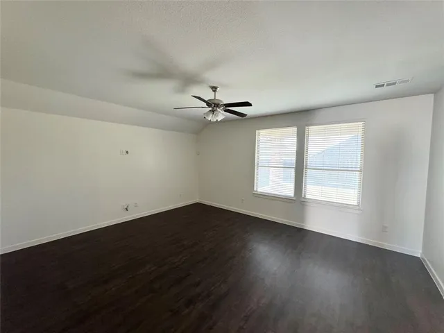 an empty room with wooden floor fan and windows