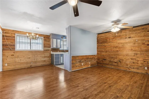 an empty room with wooden floor chandelier fan and windows