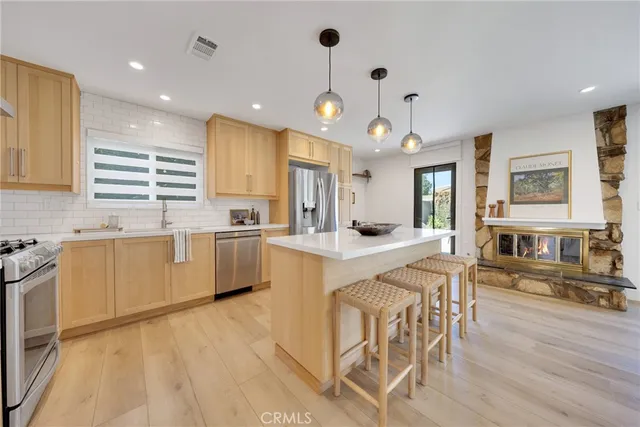 a kitchen with stainless steel appliances kitchen island granite countertop a stove a sink a refrigerator and white cabinets with wooden floor