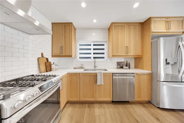 a kitchen with stainless steel appliances granite countertop a stove a sink dishwasher and a refrigerator with wooden floor