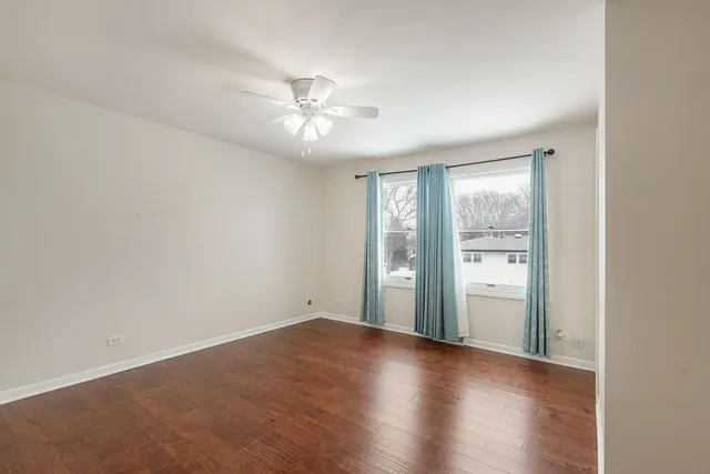 an empty room with wooden floor fan and windows