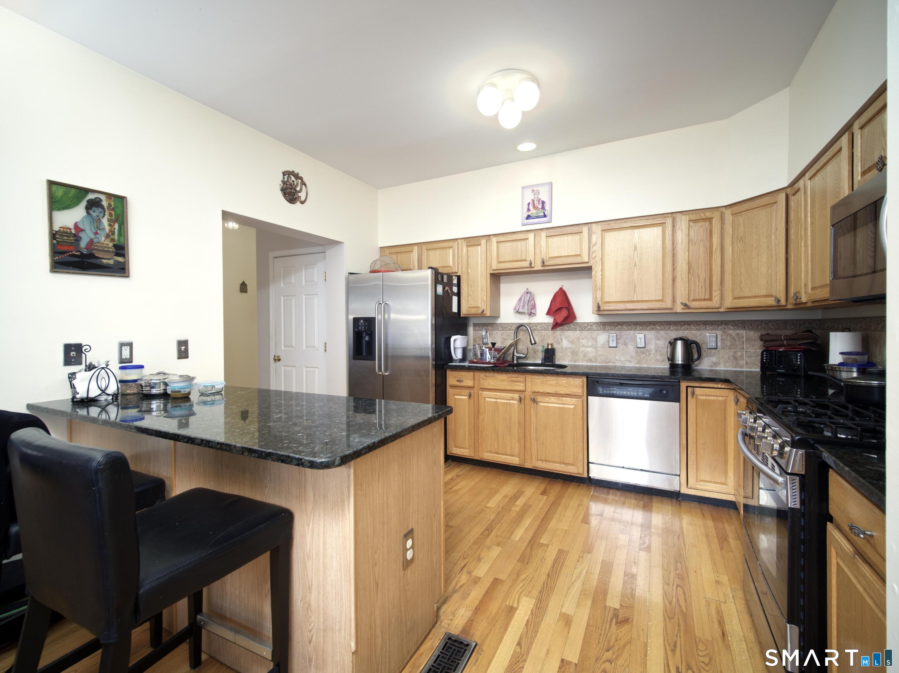 65 Benton Street, Unit 65 Fairfield, CT 06825 - Photo 8 of 35 a kitchen with stainless steel appliances granite countertop a sink dishwasher a refrigerator a microwave oven with cabinets and wooden floor