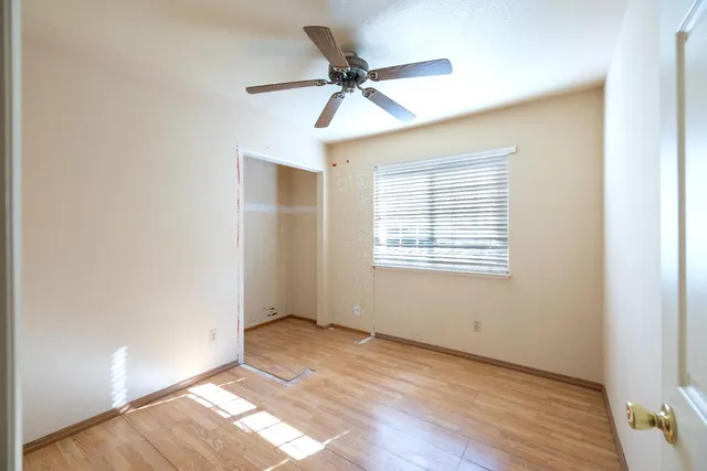 an empty room with wooden floor fan and windows