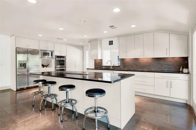 a kitchen with stainless steel appliances granite countertop a stove a sink a refrigerator and white cabinets with wooden floor