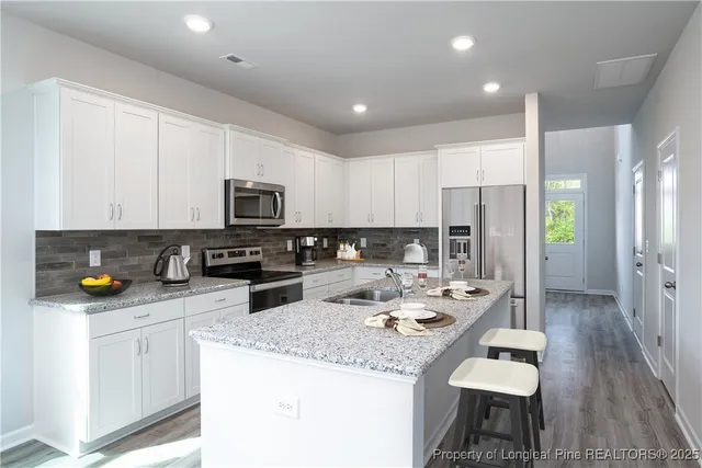 a kitchen with stainless steel appliances kitchen island granite countertop a refrigerator a stove a sink a dining table and chairs