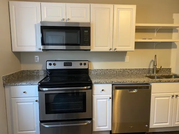 a kitchen with stainless steel appliances granite countertop white cabinets and a stove top oven