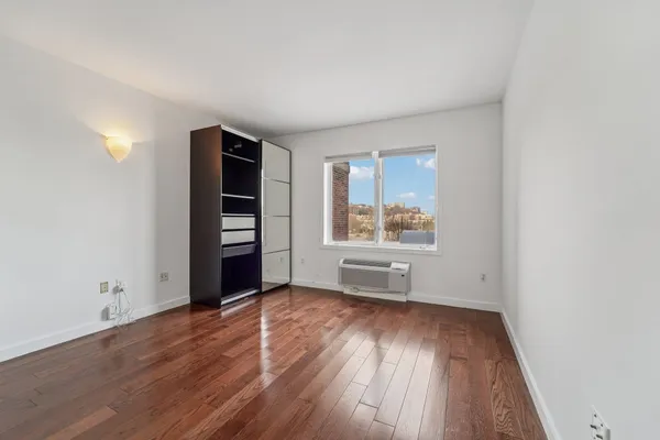 an empty room with wooden floor closet and windows