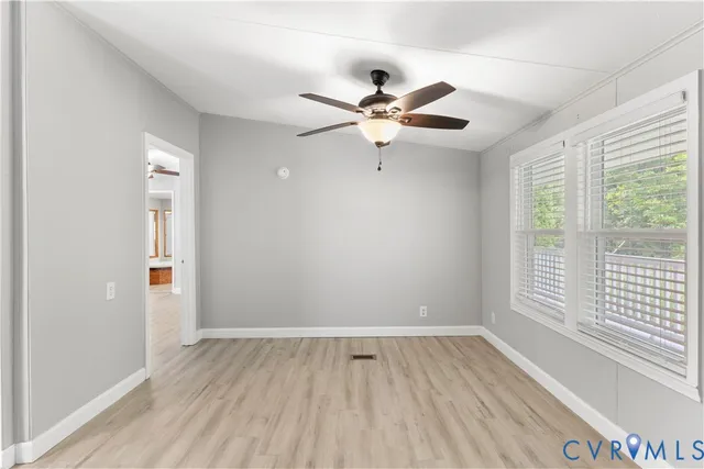 an empty room with wooden floor fan and windows
