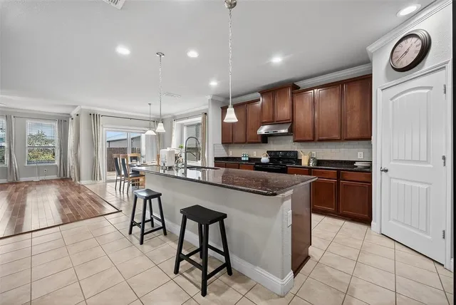 a kitchen with stainless steel appliances granite countertop a stove top oven a sink a dining table and chairs with wooden floor