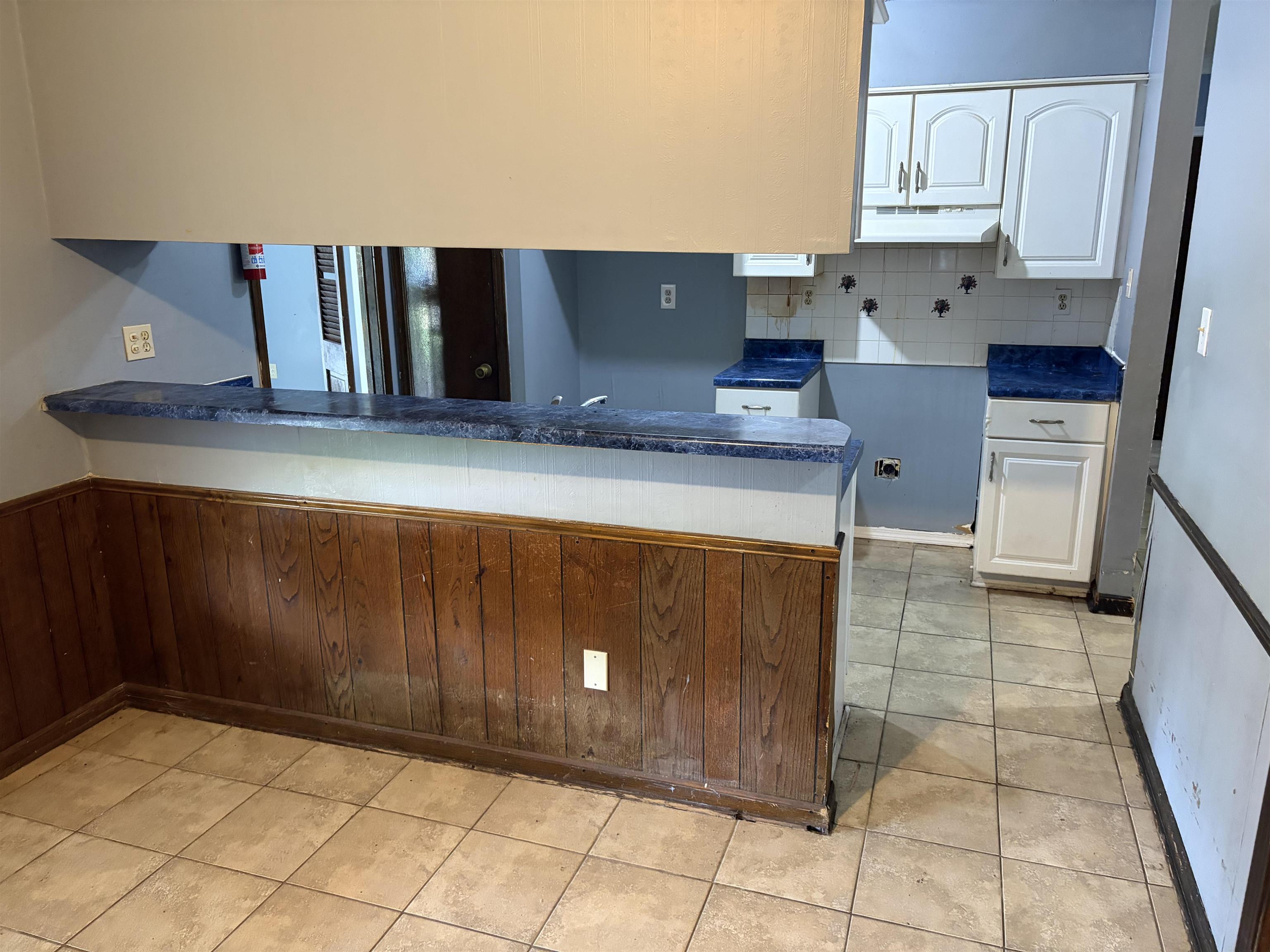 4993 Cedar View Road Memphis, TN 38118 - Photo 20 of 23 Kitchen area featuring a pass-through window, wood-finish wainscoting, white upper and lower cabinetry, blue countertops, and a white tile backsplash