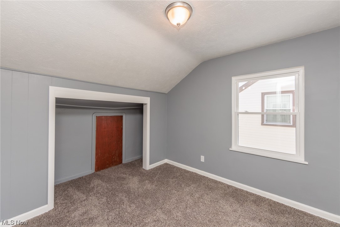 3880 Strandhill Road Cleveland, OH 44128 - Photo 22 of 33 Additional living space featuring a textured ceiling, vaulted ceiling, and dark colored carpet