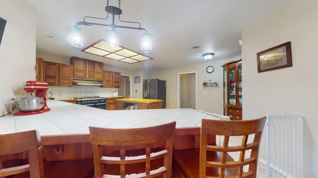 a kitchen with stainless steel appliances granite countertop a stove a refrigerator a kitchen island a dining table and chairs with wooden floor