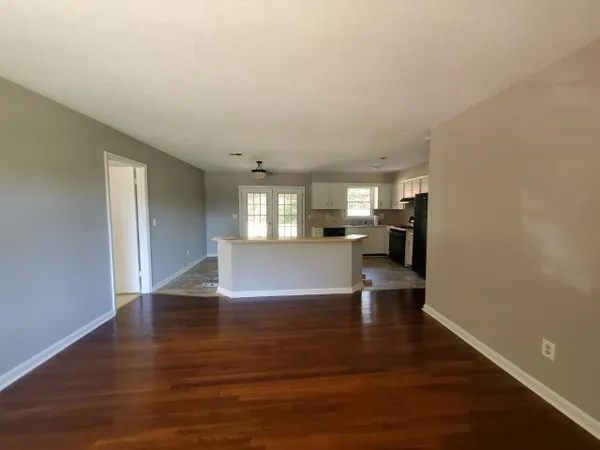 a view of an empty room and kitchen with wooden floor