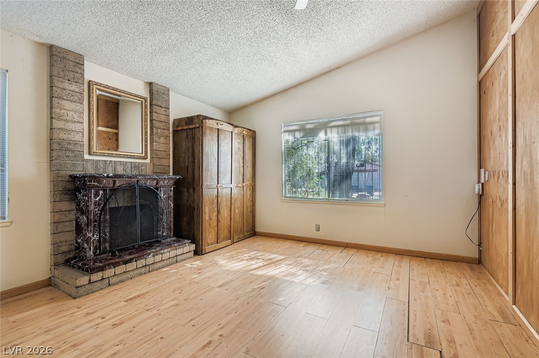 4723 Desert Vista Road Las Vegas, NV 89121 - Photo 5 of 29 Unfurnished living room featuring vaulted ceiling, a textured ceiling, a brick fireplace, and light wood-style flooring