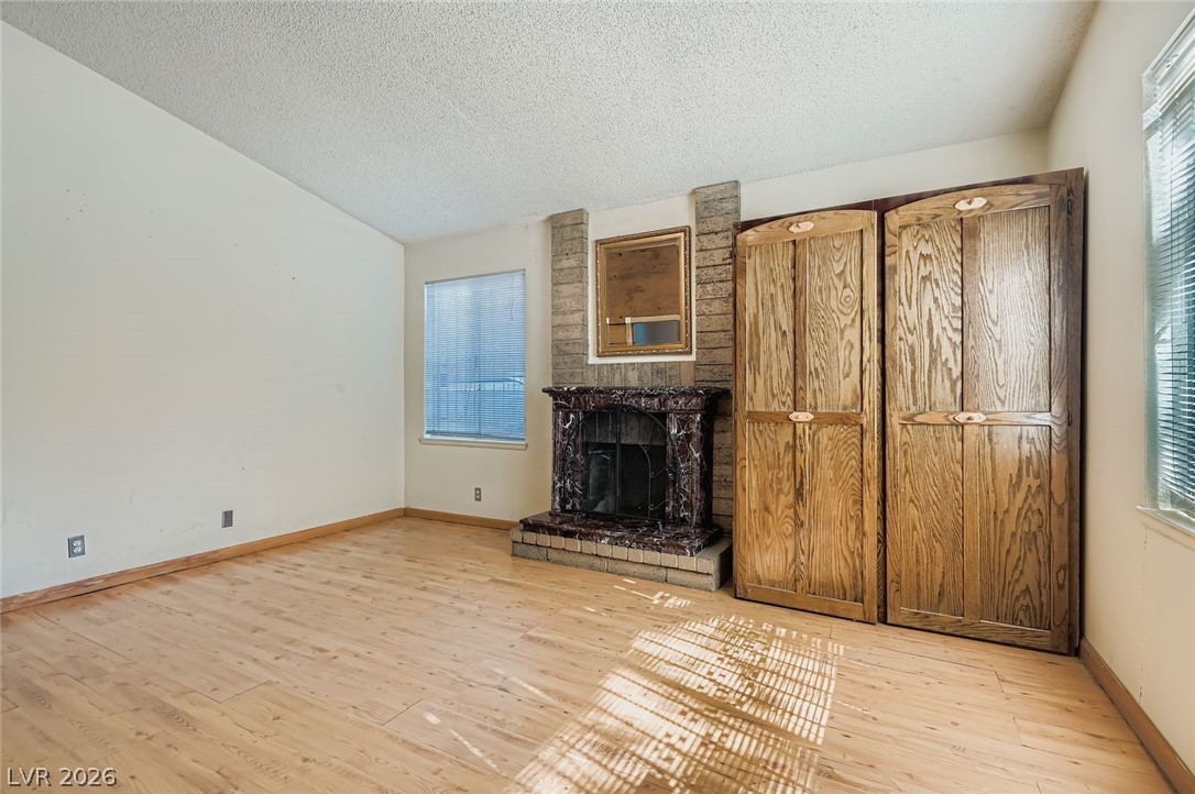4723 Desert Vista Road Las Vegas, NV 89121 - Photo 7 of 29 Unfurnished living room featuring wood finished floors, a textured ceiling, lofted ceiling, and a brick fireplace