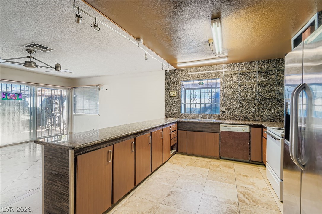 4723 Desert Vista Road Las Vegas, NV 89121 - Photo 8 of 29 Kitchen featuring a textured ceiling, a peninsula, stainless steel fridge, rail lighting, and dishwashing machine