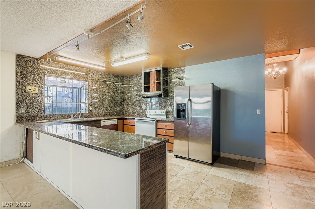 4723 Desert Vista Road Las Vegas, NV 89121 - Photo 9 of 29 Kitchen with rail lighting, a textured ceiling, a peninsula, stainless steel fridge with ice dispenser, and white electric range