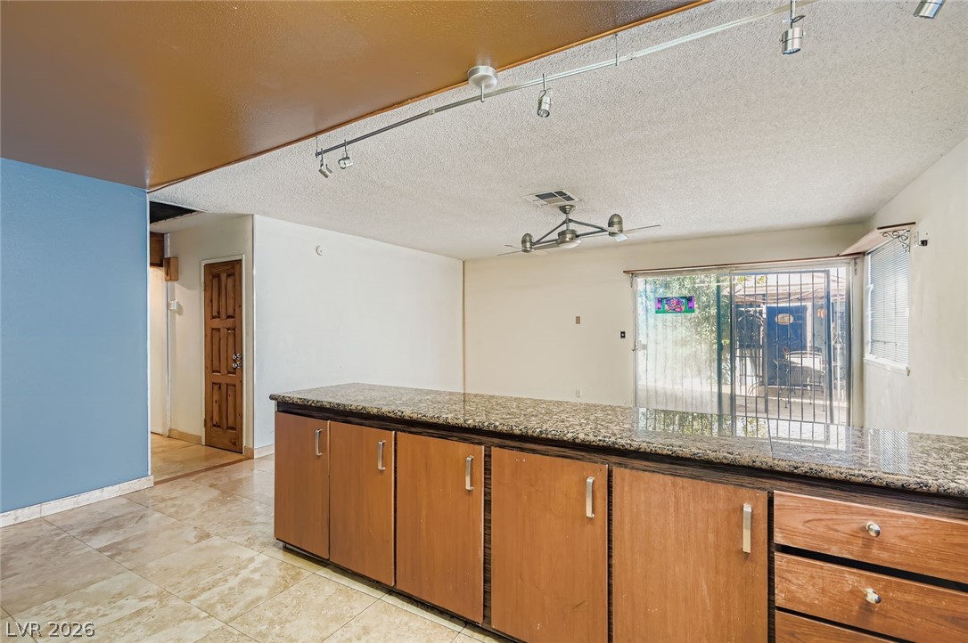 4723 Desert Vista Road Las Vegas, NV 89121 - Photo 10 of 29 Kitchen featuring a textured ceiling, stone countertops, and brown cabinets