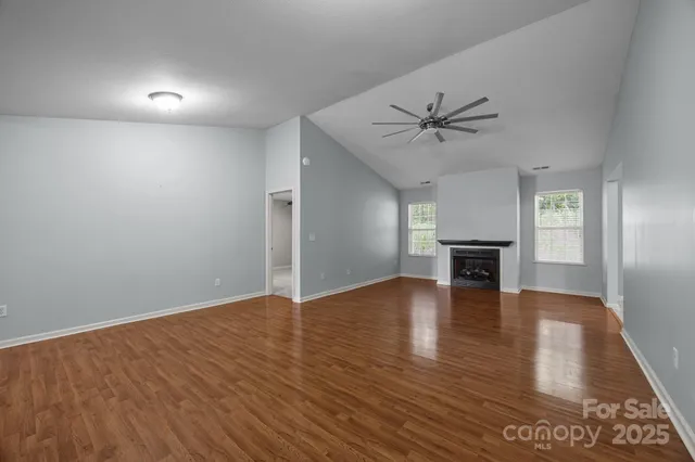 an empty room with wooden floor a ceiling fan and windows