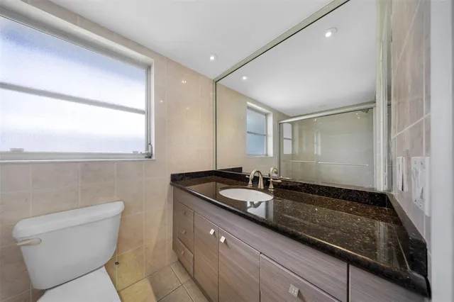 a bathroom with a granite countertop sink a toilet a mirror and shower