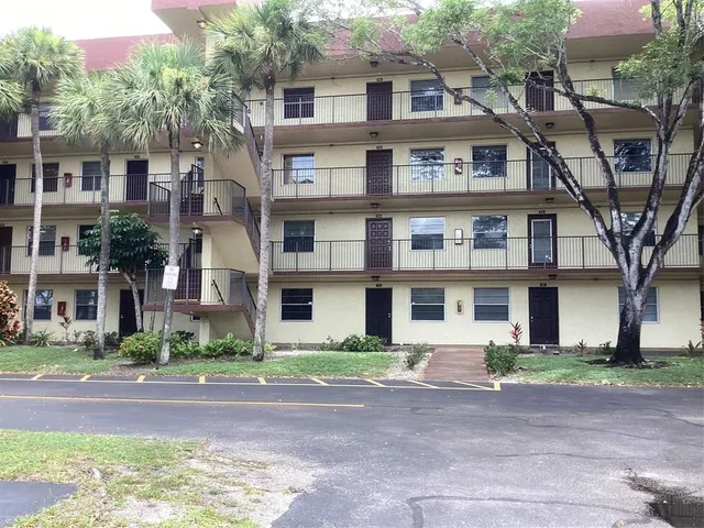 a front view of a residential apartment building with yard and parking
