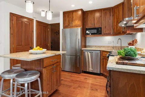 a kitchen with stainless steel appliances granite countertop a kitchen island hardwood floor and a refrigerator