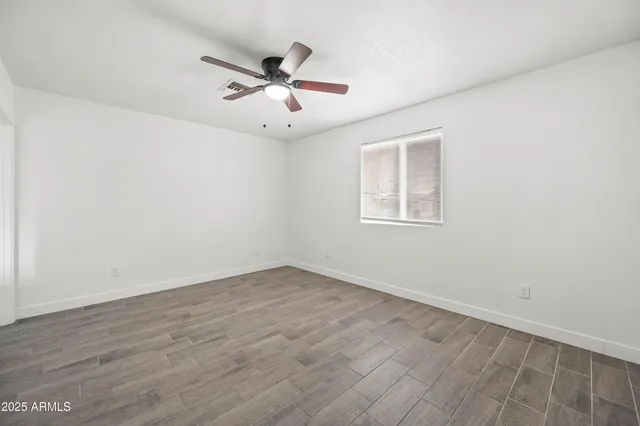 an empty room with wooden floor fan and windows