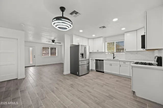 a kitchen with stainless steel appliances granite countertop a refrigerator a sink dishwasher a stove and white countertops with wooden floor