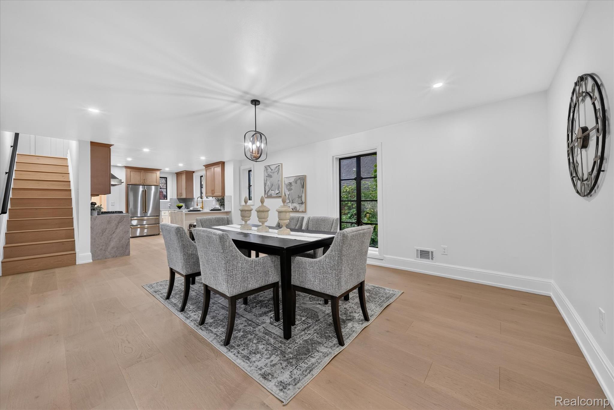 3250 Sherbourne Road Detroit, MI 48221 - Photo 11 of 36 Open-concept living area featuring light wood-finish flooring, a kitchen with wood cabinetry and stainless steel appliances, and a dining area illuminated by a modern chandelier