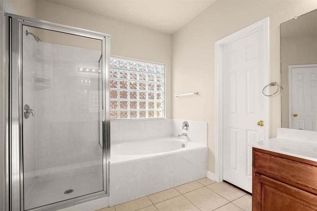 10105 Wind Cave Trail Austin, TX 78747 - Photo 12 of 23 Spacious bathroom featuring a glass-enclosed shower, built-in bathtub, glass block window, wood-finish vanity with countertop, and tile flooring