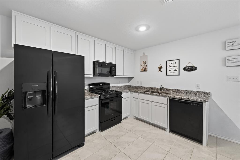 464 Reverie Way Ferris, TX 75125 - Photo 10 of 36 White shaker-style cabinetry, dark speckled countertops, stainless steel sink, black range with an overhead microwave, and integrated black dishwasher