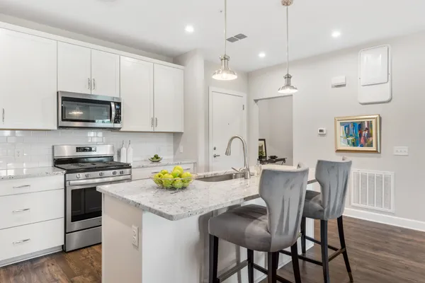 a kitchen with stainless steel appliances granite countertop a stove a sink a microwave a refrigerator white cabinets and wooden floor