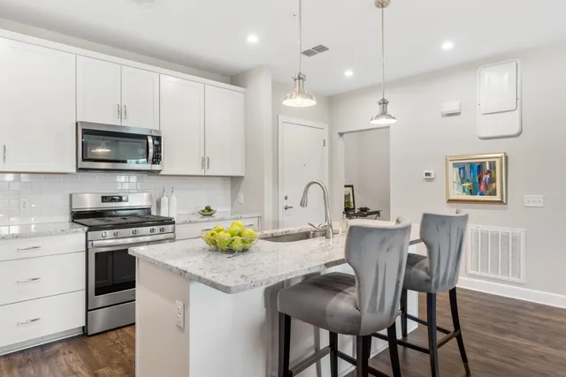 a kitchen with stainless steel appliances granite countertop a stove a sink a microwave a refrigerator white cabinets and wooden floor