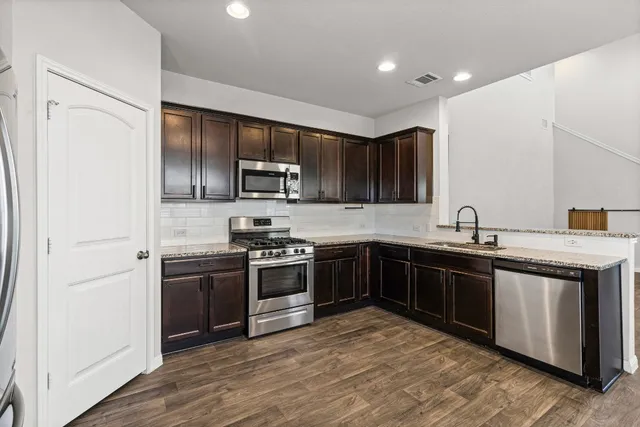 a kitchen with stainless steel appliances granite countertop a stove top oven a sink and dishwasher a refrigerator with wooden floor