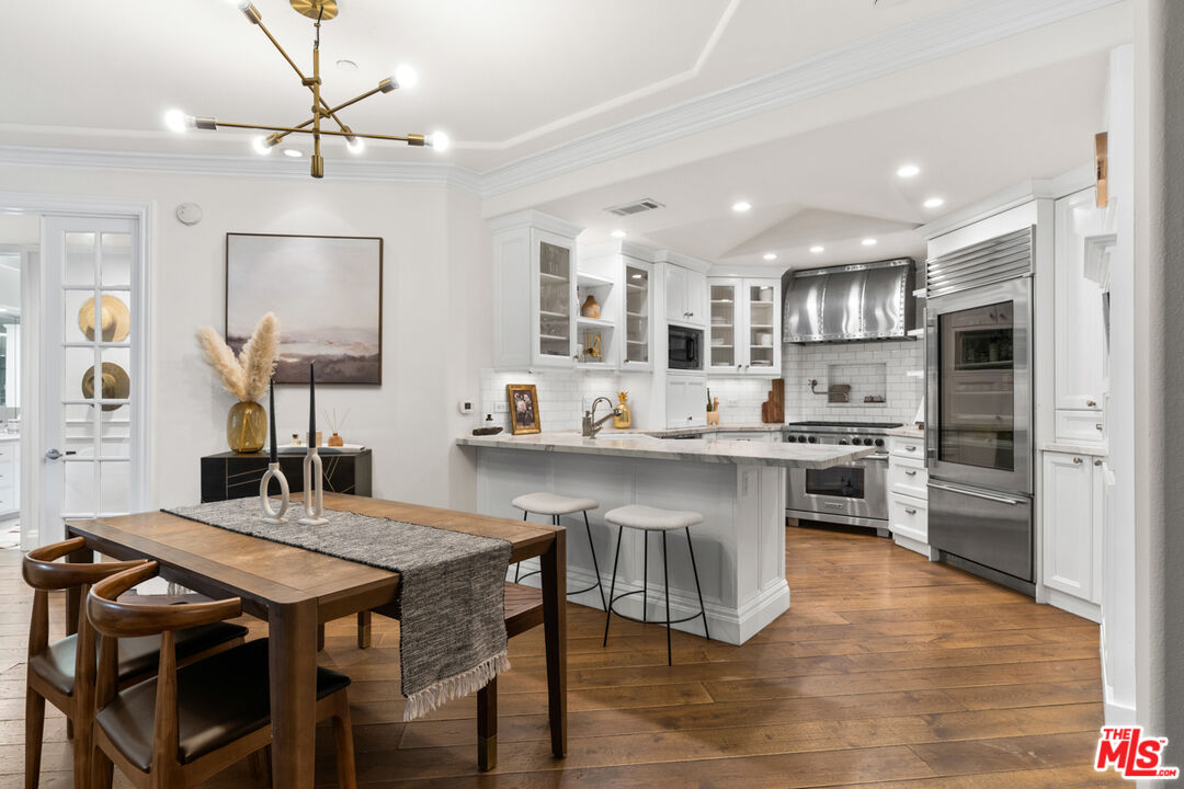 a kitchen with stainless steel appliances granite countertop a stove a refrigerator a sink dishwasher a dining table and chairs with wooden floor