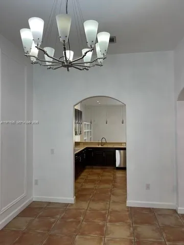 a room with a chandelier fan and kitchen view