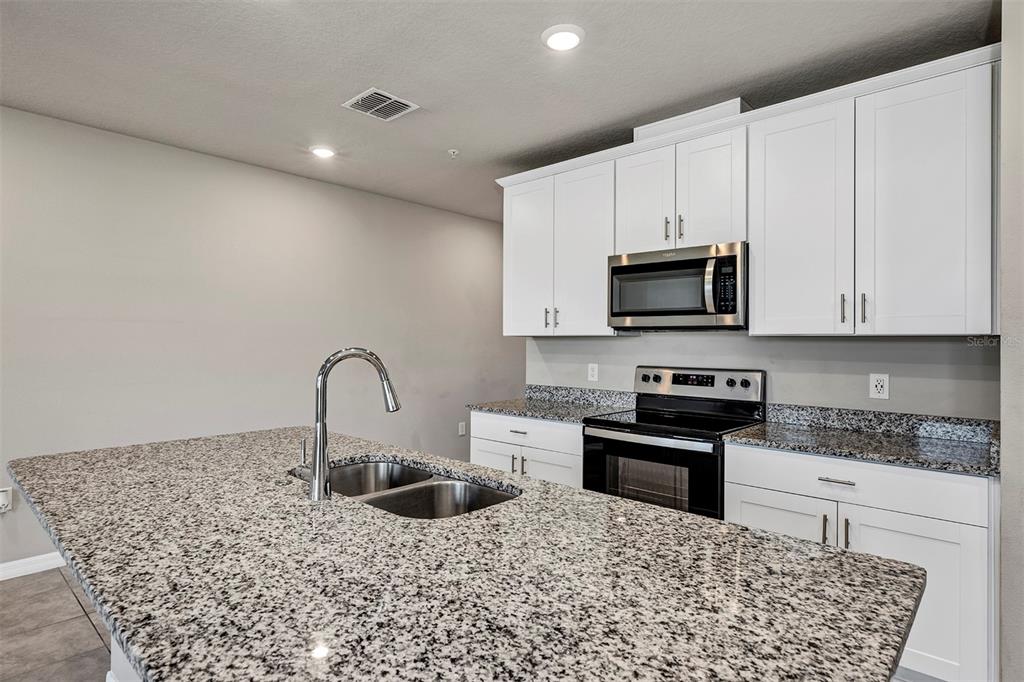 1073 Desert Candle Drive Ocoee, FL 34761 - Photo 10 of 55 a kitchen with stainless steel appliances kitchen island granite countertop a sink a stove a microwave and cabinets