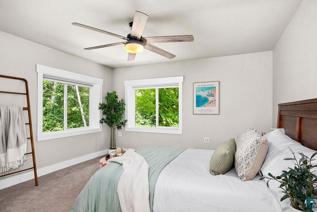 5025 Reid Road Duluth, MN 55803 - Photo 24 of 51 Carpeted bedroom featuring two large windows with white trim, a ceiling fan with light fixture, and a dark wood headboard