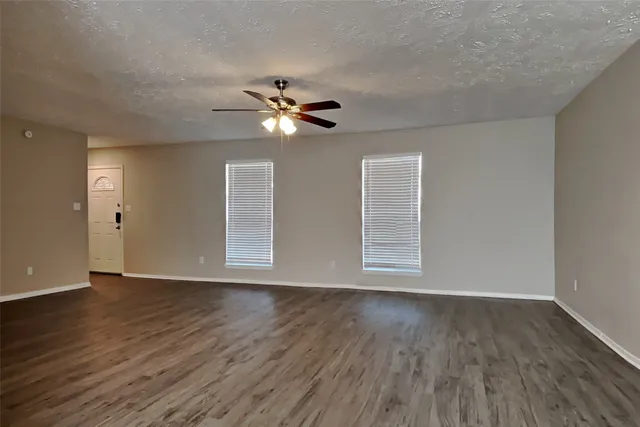 a view of an empty room with wooden floor and a ceiling fan
