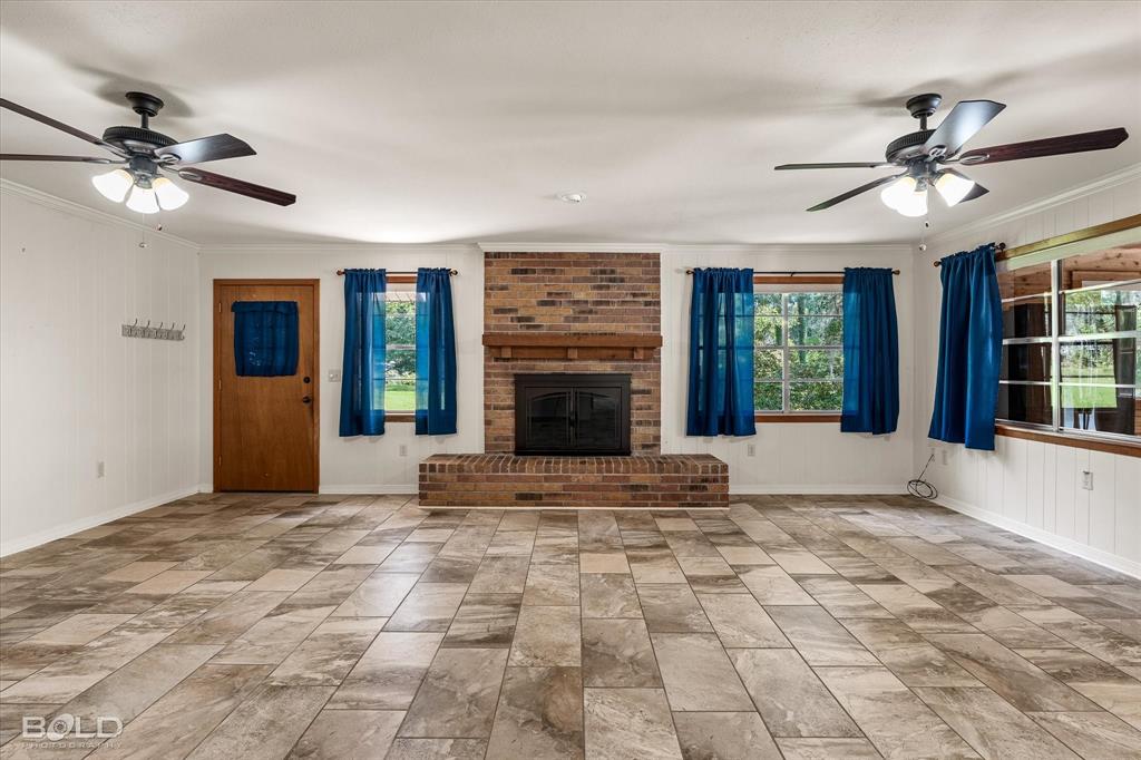 225 Marie Road Ringgold, LA 71068 - Photo 19 of 40 Expansive living area featuring large format tile flooring, a brick fireplace with a wood mantel, two ceiling fans with integrated lighting, and multiple windows
