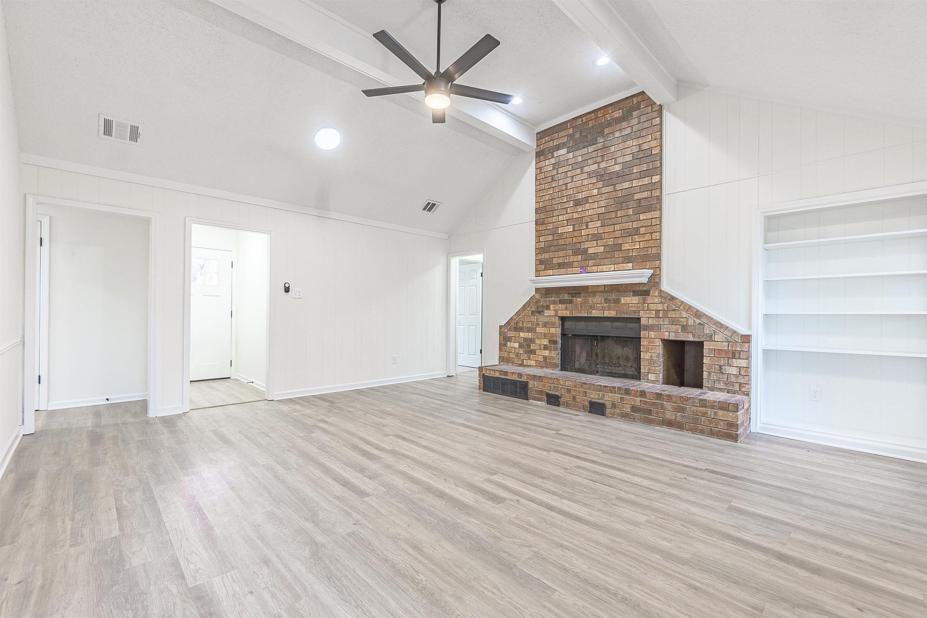 6538 Castle Ridge Cove Memphis, TN 38141 - Photo 3 of 27 Unfurnished living room featuring built in shelves, ceiling fan, lofted ceiling with beams, a fireplace, and light hardwood / wood-style floors