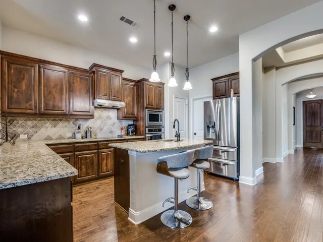 a kitchen with stainless steel appliances granite countertop a sink a stove a refrigerator and island with wooden floor