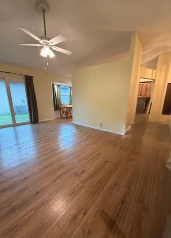 a view of an empty room with wooden floor and a ceiling fan