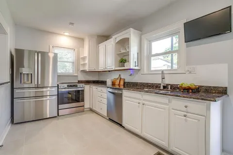 a kitchen with granite countertop a refrigerator sink and white cabinets
