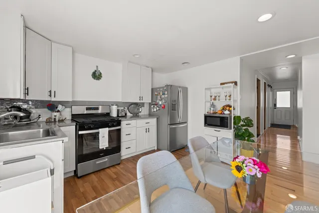 a kitchen with stainless steel appliances kitchen island granite countertop a stove a sink dishwasher and white cabinets with wooden floor