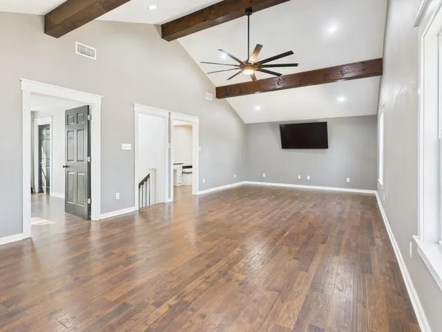 a view of an empty room with wooden floor and a ceiling fan