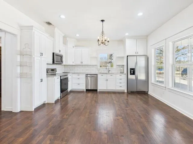 a large kitchen with stainless steel appliances kitchen island a stove a refrigerator a oven and white cabinets with wooden floor