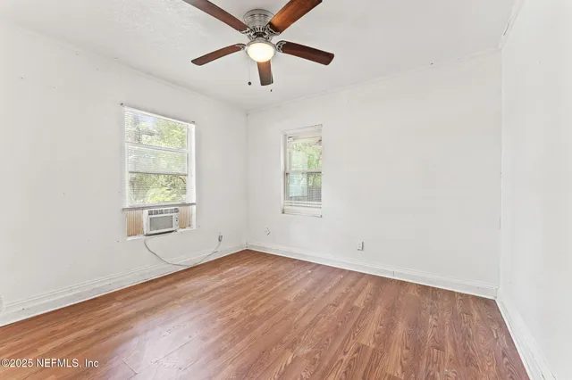an empty room with wooden floor fan and windows
