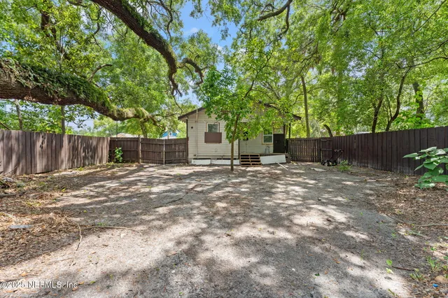 a backyard of a house with large trees and wooden fence