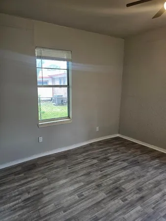 a view of an empty room with wooden floor and a window